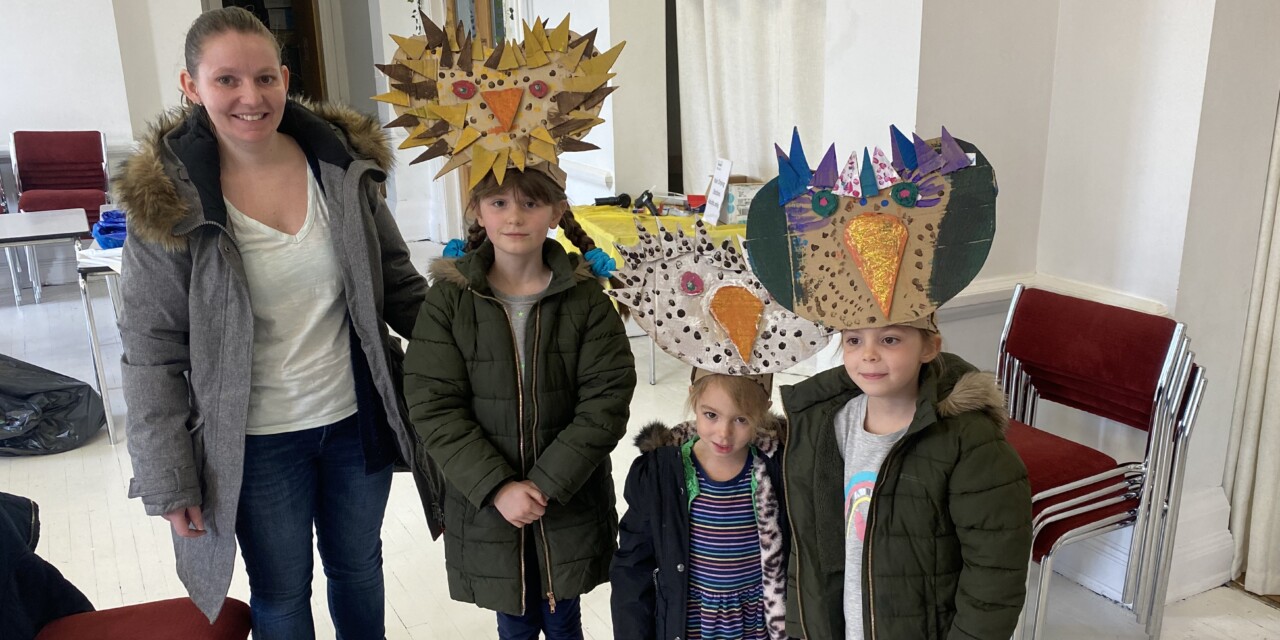 A woman stands next to three young girls, each of whom is wearing an owl mask crafted out of cardboard and painted.