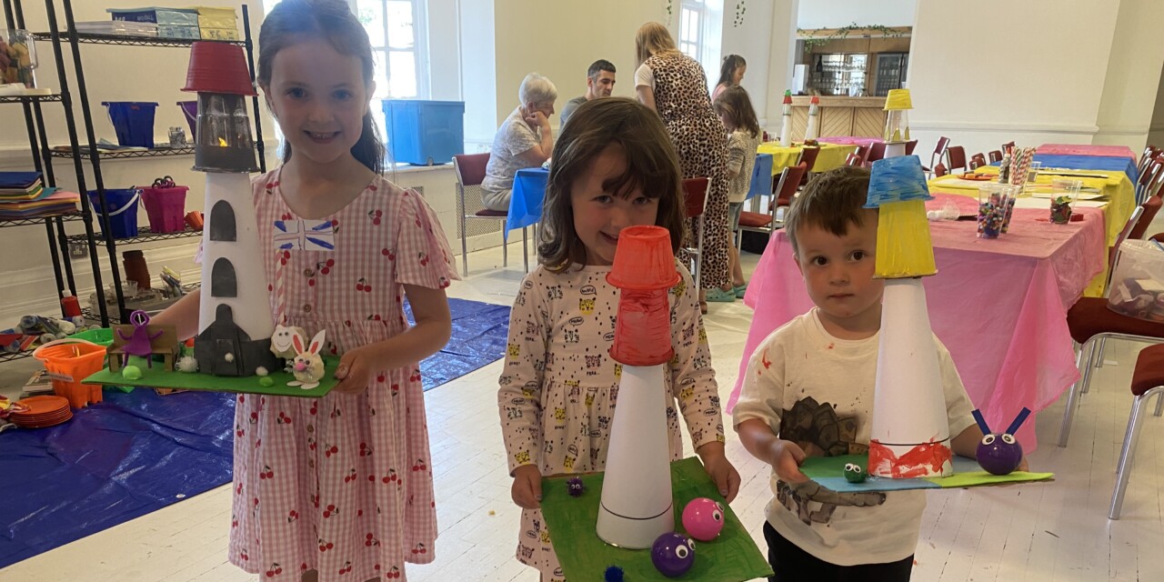 Three children (two girls, one boy) are holding up their crafted mini Hoad monuments made out of cardboard and plastic and painted.
